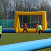 Overzicht van de opblaasbare voetbalboarding 6vs6 op een sportveld, met kinderen langs de zijlijn en een gele goal aan de andere kant.