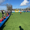 Voetbalboarding 6vs6 – Compleet voetbalveld opblaasbaar (overzicht) Overzicht van de opblaasbare voetbalboarding 6vs6 op een sportveld, met kinderen langs de zijlijn en een gele goal aan de andere kant.