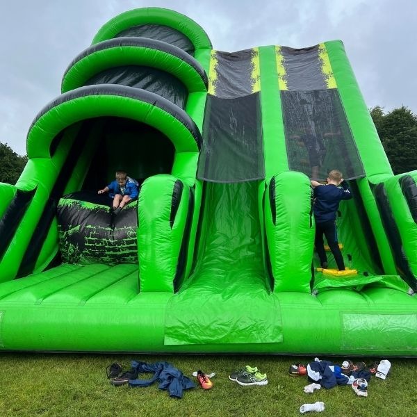 Groot groen-zwart Basejump & Slide springkussen met dubbele hoge glijbaan, ideaal voor verhuur op evenementen en kinderfeesten.
