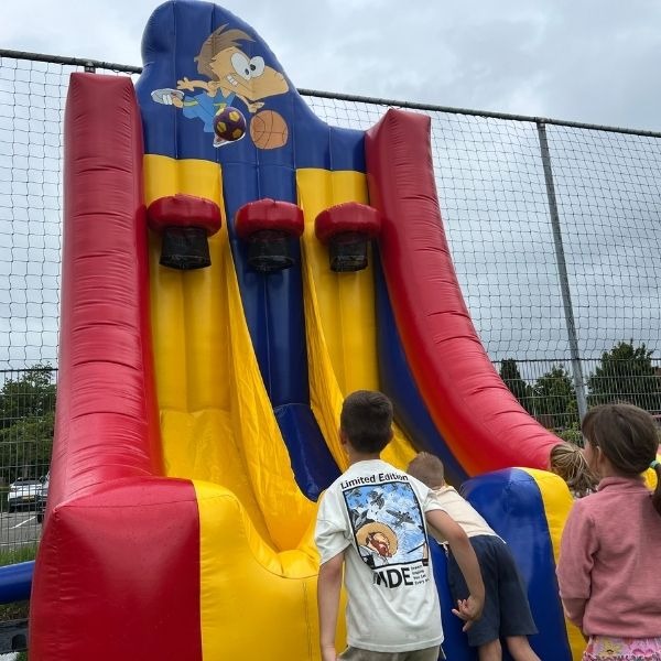Basketbal Groot – Opblaasbare basketbal attractie Opblaasbare Basketbal Groot attractie in rood, geel en blauw met drie basketballingen aan de bovenkant, geschikt voor sportieve evenementen en verhuur.