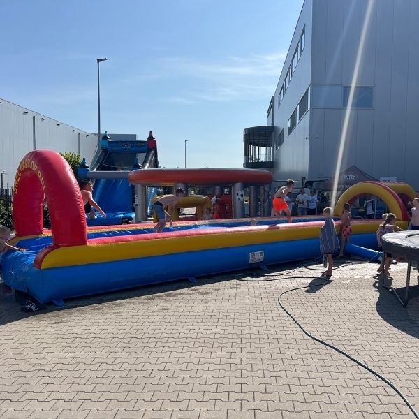 Lange opblaasbare buikschuifbaan van 15 meter met kleurrijke bogen en waterstrook.