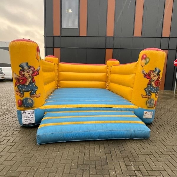 Geel-blauw springkussen met clownillustraties in circusstijl, ideaal voor verhuur op kinderfeestjes en buurtactiviteiten.