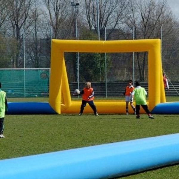 Overzicht van de opblaasbare voetbalboarding 6vs6 op een sportveld, met kinderen langs de zijlijn en een gele goal aan de andere kant.