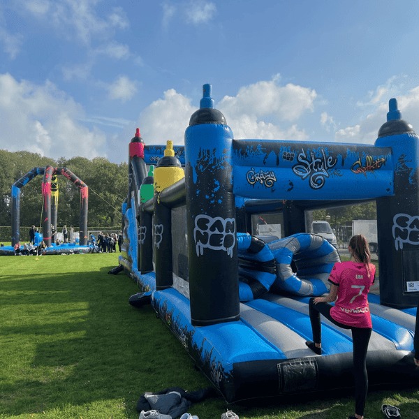 Opblaasbare graffiti stormbaan van 18 meter lang met grote klimhelling en blauwe accenten, gefotografeerd recht van voren.