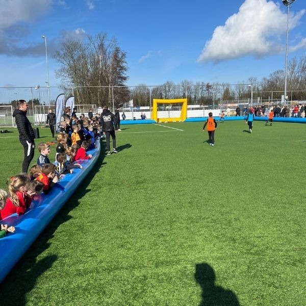 Voetbalboarding 6vs6 – Compleet voetbalveld opblaasbaar (overzicht) Overzicht van de opblaasbare voetbalboarding 6vs6 op een sportveld, met kinderen langs de zijlijn en een gele goal aan de andere kant.